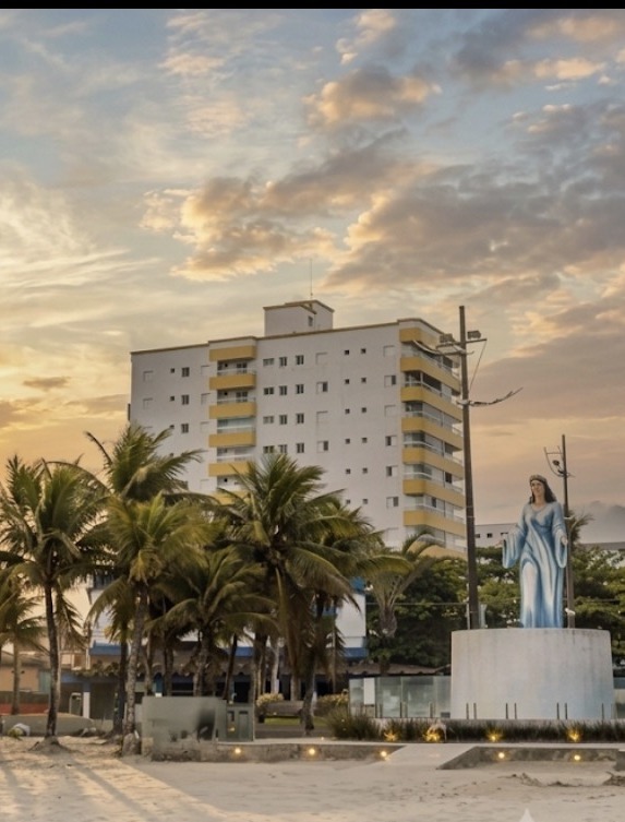 Prédio residencial branco com varandas amarelas frente-mar em Praia Grande, na Av. 23 de Maio, ao lado da estátua de Iemanjá, ao pôr do sol.